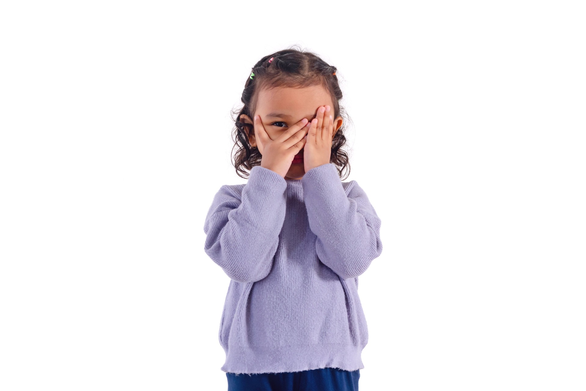 A little Asian girl covers her face with her hands and peeks between her fingers